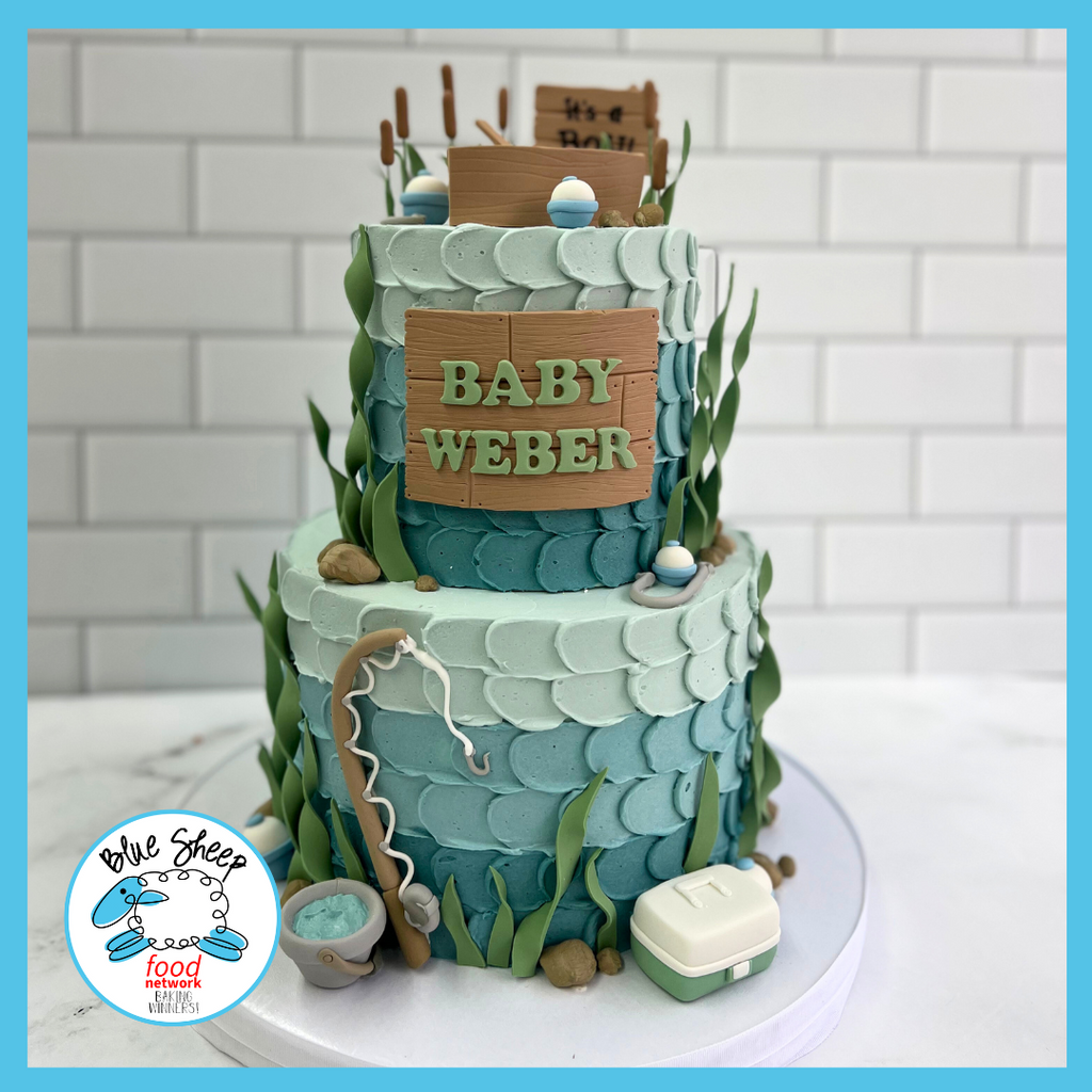 Two-tiered blue baby shower cake with a fishing theme, featuring decorations like a tackle box, fishing rod, and 'Baby Weber' sign.