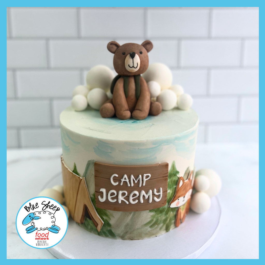Customized 'Camp Jeremy' birthday cake featuring a hand-painted camping scene, fondant bear topper, and marshmallow details on a forest-inspired base.