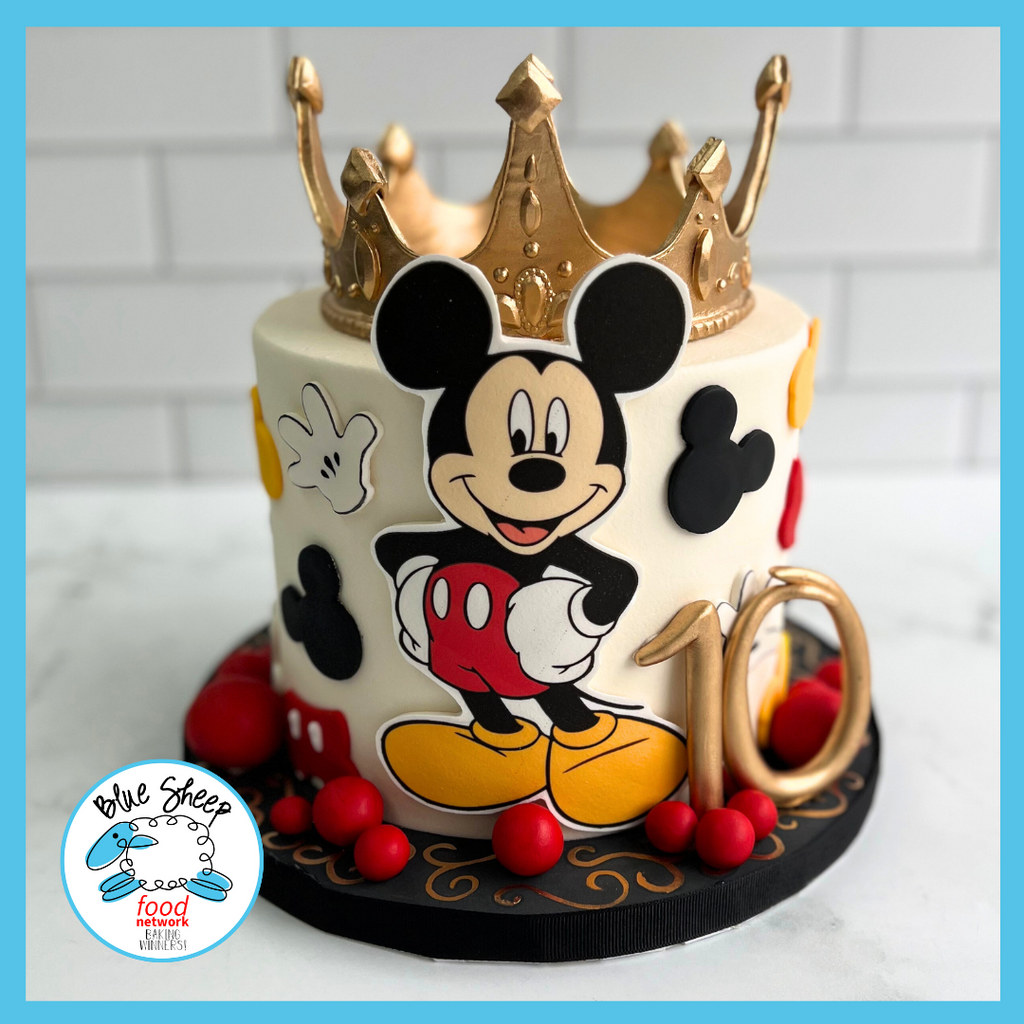 Children's birthday cake with an iconic cartoon character, featuring a golden crown topper, and vibrant fondant decorations on a white backdrop.