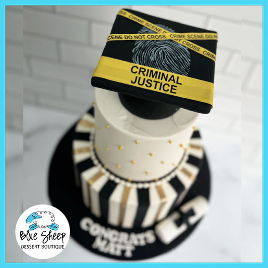 A graduation cake with a criminal justice theme, featuring black and white stripes, yellow 'CRIME SCENE DO NOT CROSS' tape, and a graduation cap with 'CRIMINAL JUSTICE' on the board.