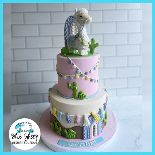 Llama themed custom birthday cake with two tiers, featuring a llama topper, cactus decorations, and colorful bunting.