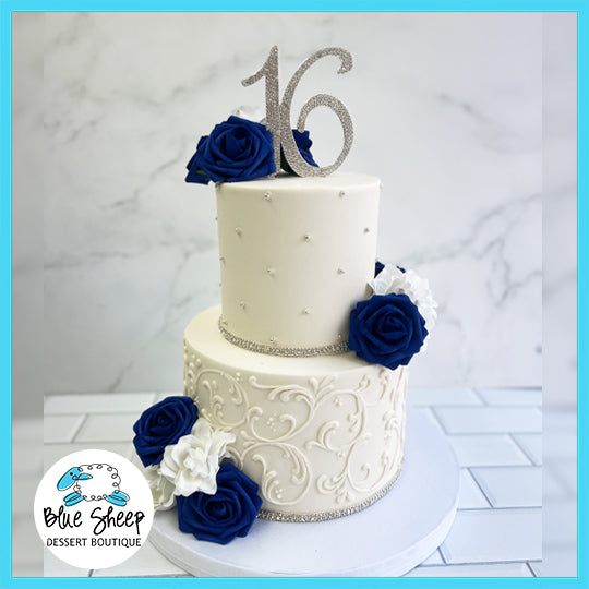 A two-tiered Sweet 16 birthday cake with silver filigree, sparkling "16" topper, and royal blue roses.