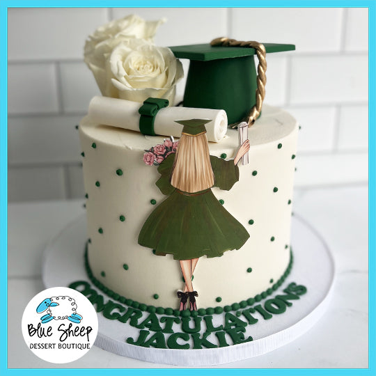 A graduation-themed cake with a green cap and diploma on top, white roses, and a girl in a green gown silhouette on the side with CONGRATULATIONS!