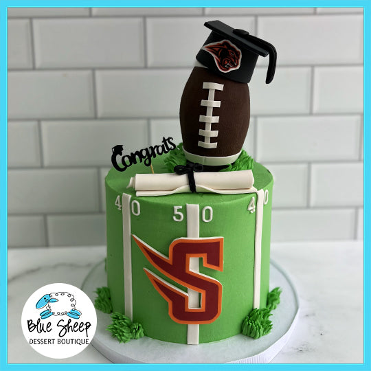 Custom green graduation cake with a football, diploma, and Susquehanna University logo topped with a graduation cap.