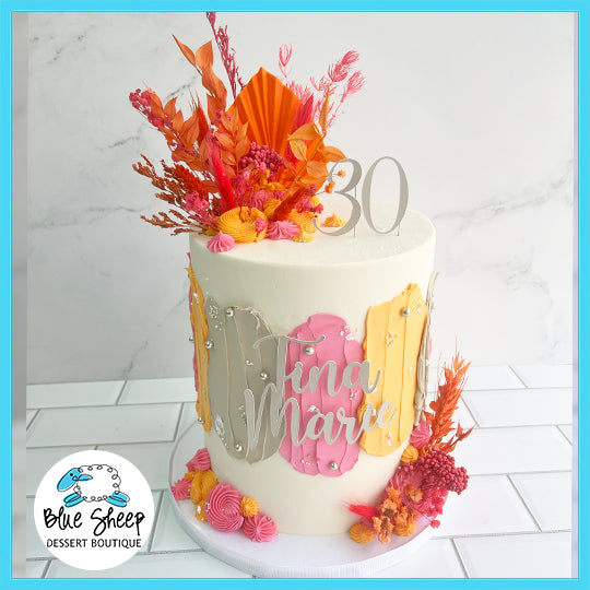 A custom 30th birthday cake with a chic 'Tina Marie' sign, adorned with orange and pink floral accents and gold details.