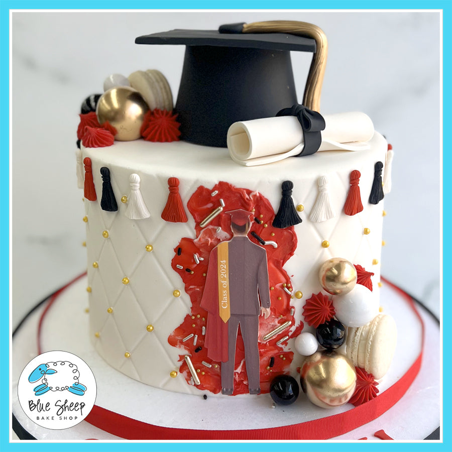 Graduation cake with quilted white design, gold accents, red and black tassels, golden spheres, macarons, graduate silhouette, graduation cap, and scroll.