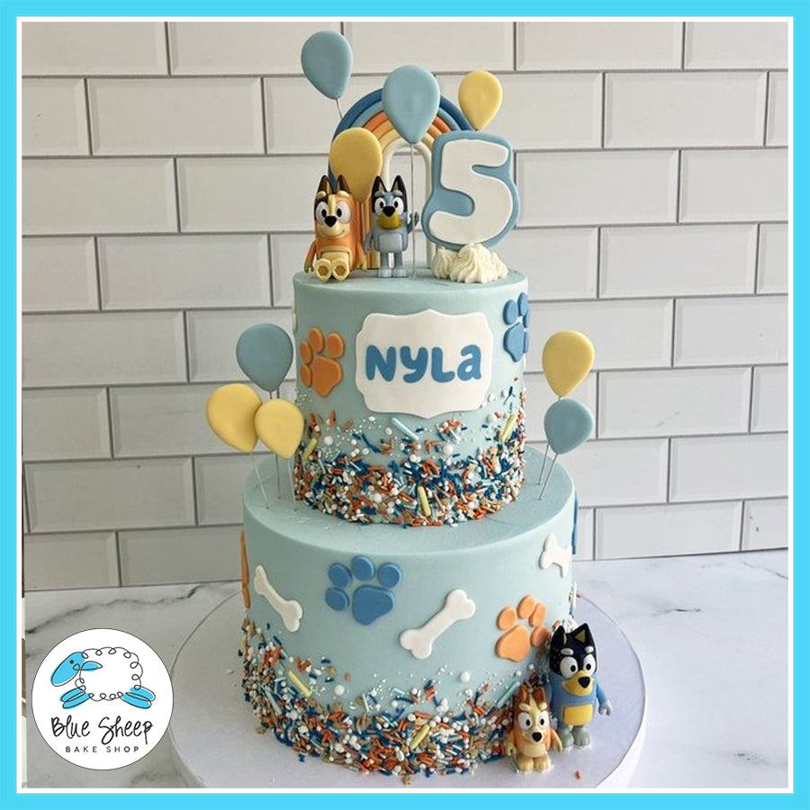 Custom Bluey-themed birthday cake with two tiers, Bluey and Bingo toppers, paw prints, dog bones, colorful balloons, and sprinkles, perfect for kids’ parties in Somerville, NJ.