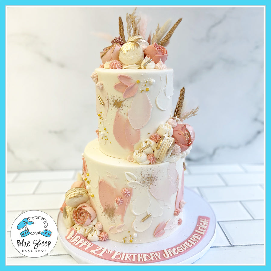 wo-tier blush and gold boho birthday cake with dried florals, macarons, and hand-painted accents.