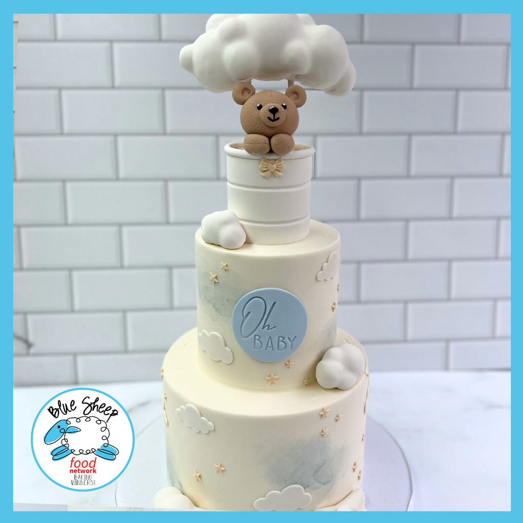 Delicate baby shower cake with a sleeping teddy bear on a cloud, 'Oh Baby' inscription, and gentle starry and cloudy decorations.