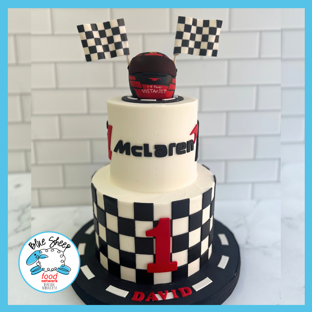 Motorsport-inspired birthday cake styled as a racing helmet on a checkered base, complete with racing team logos and personalized for a special celebration.