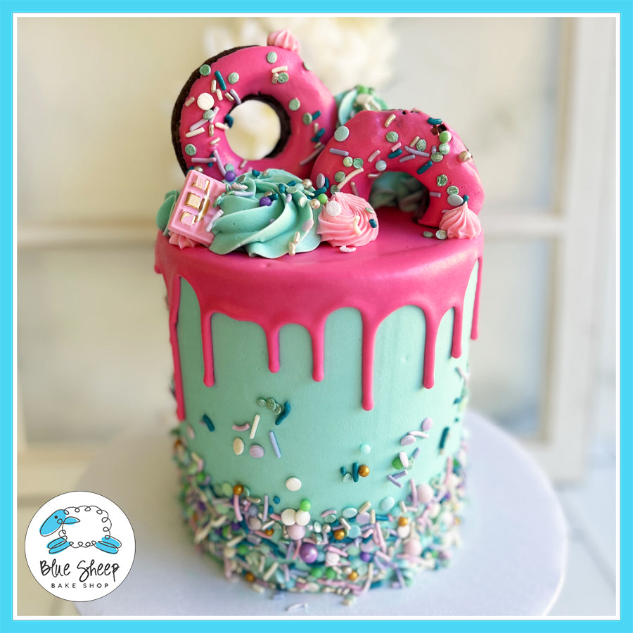 Donut-themed birthday cake with teal buttercream, pink drip, sprinkle-covered donuts, and buttercream swirls by Blue Sheep Bake Shop in Somerville, NJ.