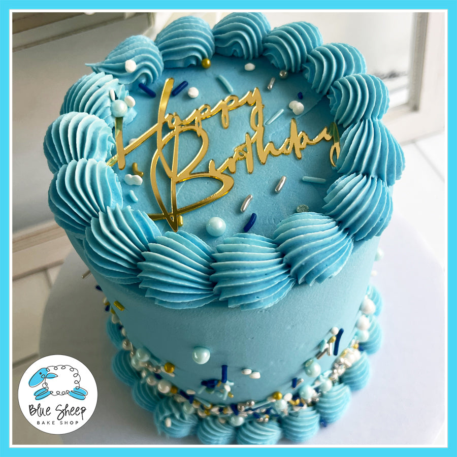 Blue buttercream birthday cake with gold "Happy Birthday" topper and pearl sprinkles by Blue Sheep Bake Shop.