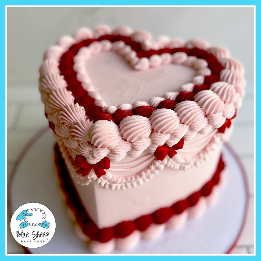 Romantic heart-shaped pink cake with red buttercream accents, vintage piping, and rosette details from Blue Sheep Bake Shop in Somerville, NJ