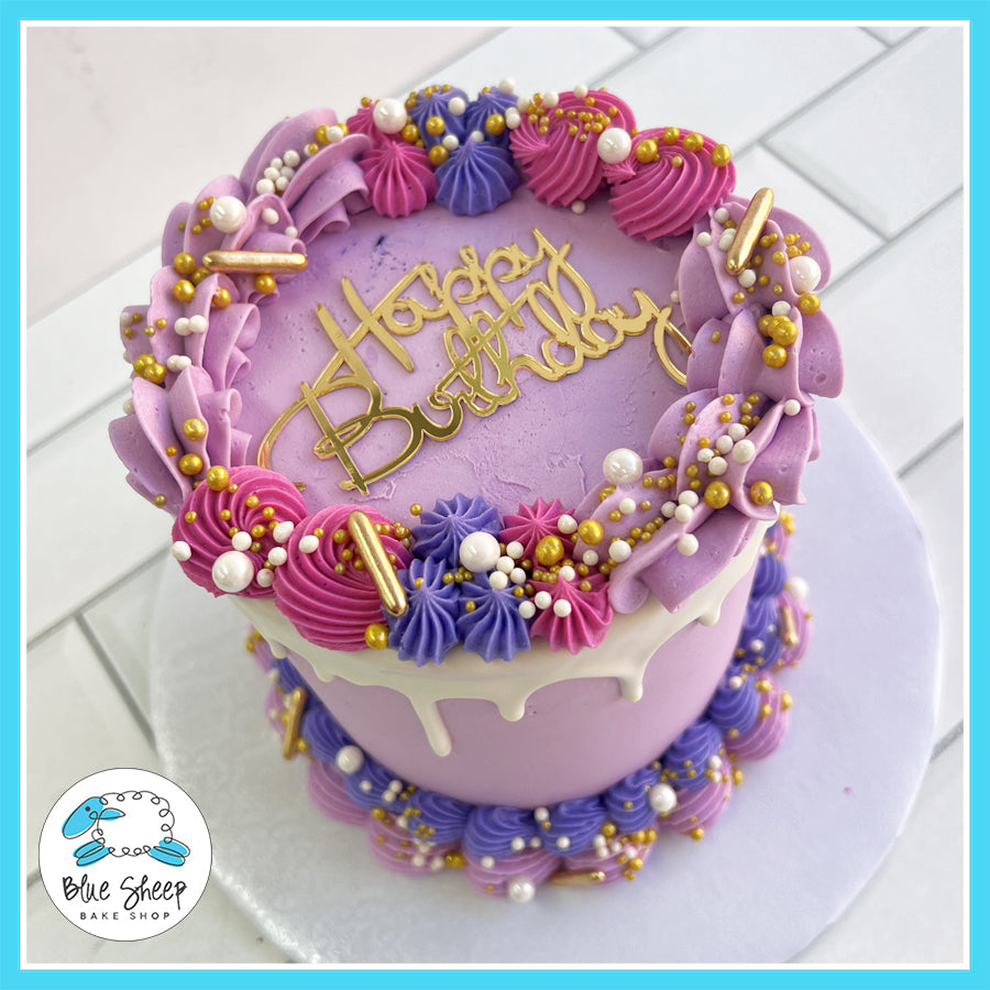 Lavish purple and pink birthday cake with white chocolate ganache drip, gold pearls, and buttercream piping, custom-made by Blue Sheep Bake Shop in Somerville, NJ.