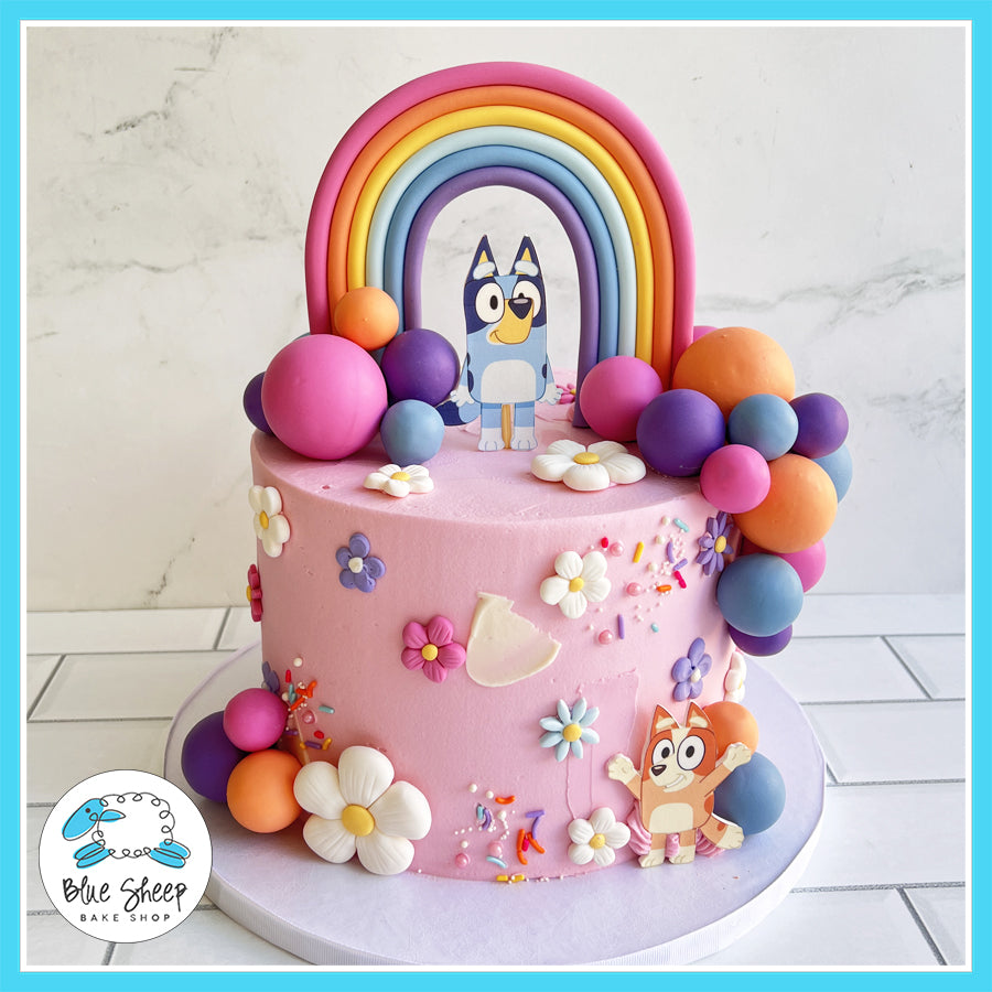 Custom Bluey-themed birthday cake with a rainbow arch, colorful balloon clusters, Bluey and Bingo toppers, and fondant flowers, perfect for kids’ parties in Somerville, NJ.