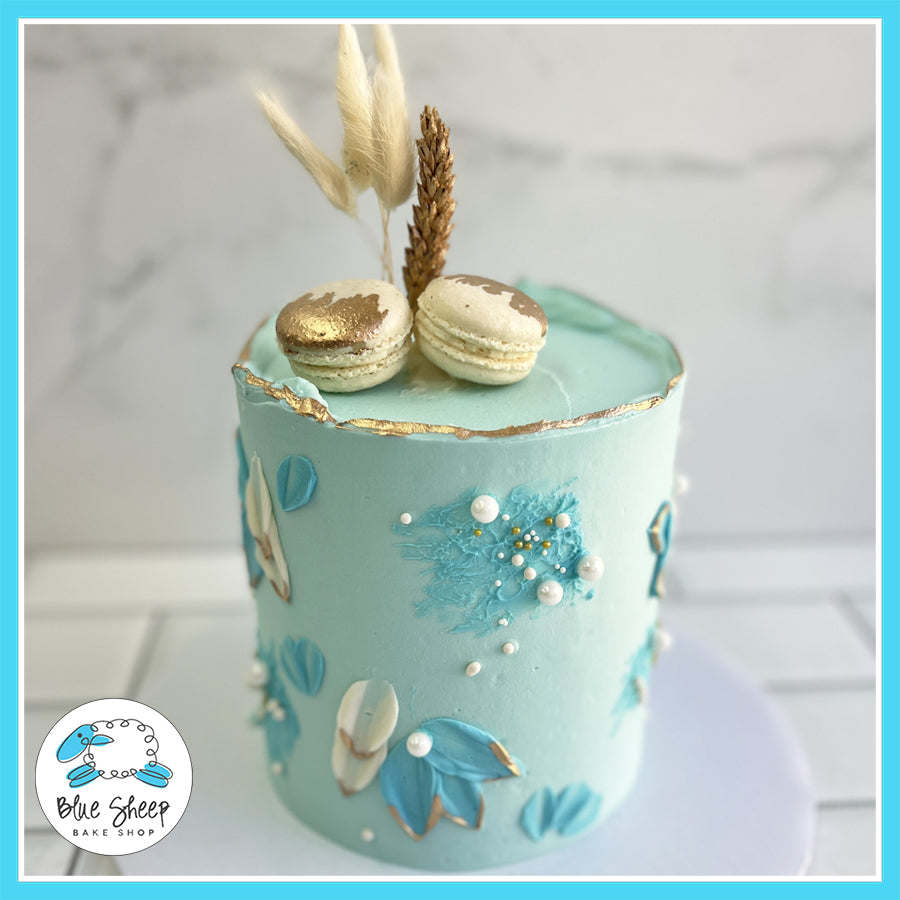 Bohemian-inspired pastel blue buttercream cake with gold accents, dried wheat, and macarons, handcrafted at Blue Sheep Bake Shop in Somerville, NJ.

