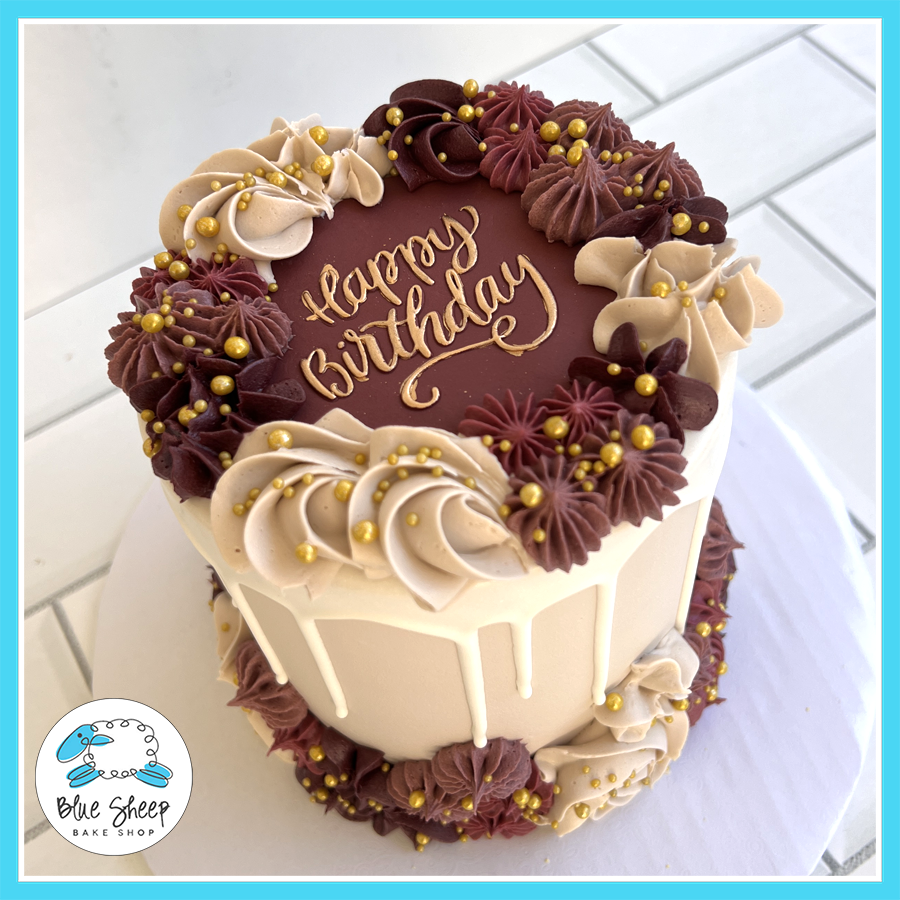 Elegant burgundy and gold birthday cake with white chocolate drip, buttercream swirls, gold pearls, and a “Happy Birthday” inscription, available at Blue Sheep Bake Shop in Somerville, NJ