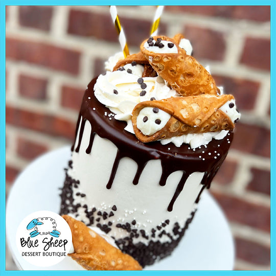 A white cake decorated with chocolate ganache drip, mini cannoli, whipped cream, and chocolate chips.