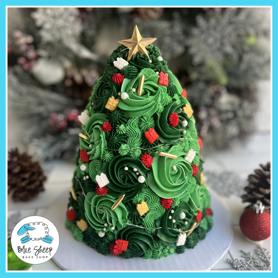 A beautifully decorated Christmas tree-shaped cake with green buttercream swirls, holiday decorations, and glowing LED lights, topped with a gold star.