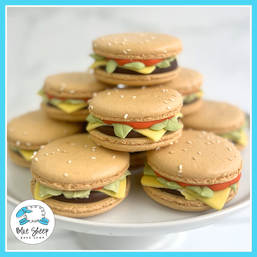 Burger macarons with fondant lettuce, cheese, and tomato layers, designed to look like mini burgers.