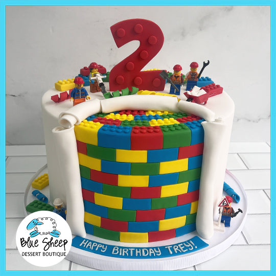 Custom LEGO-themed birthday cake with colorful brick design and mini-figures, topped with a large number 2, delivered by Blue Sheep Dessert Boutique.