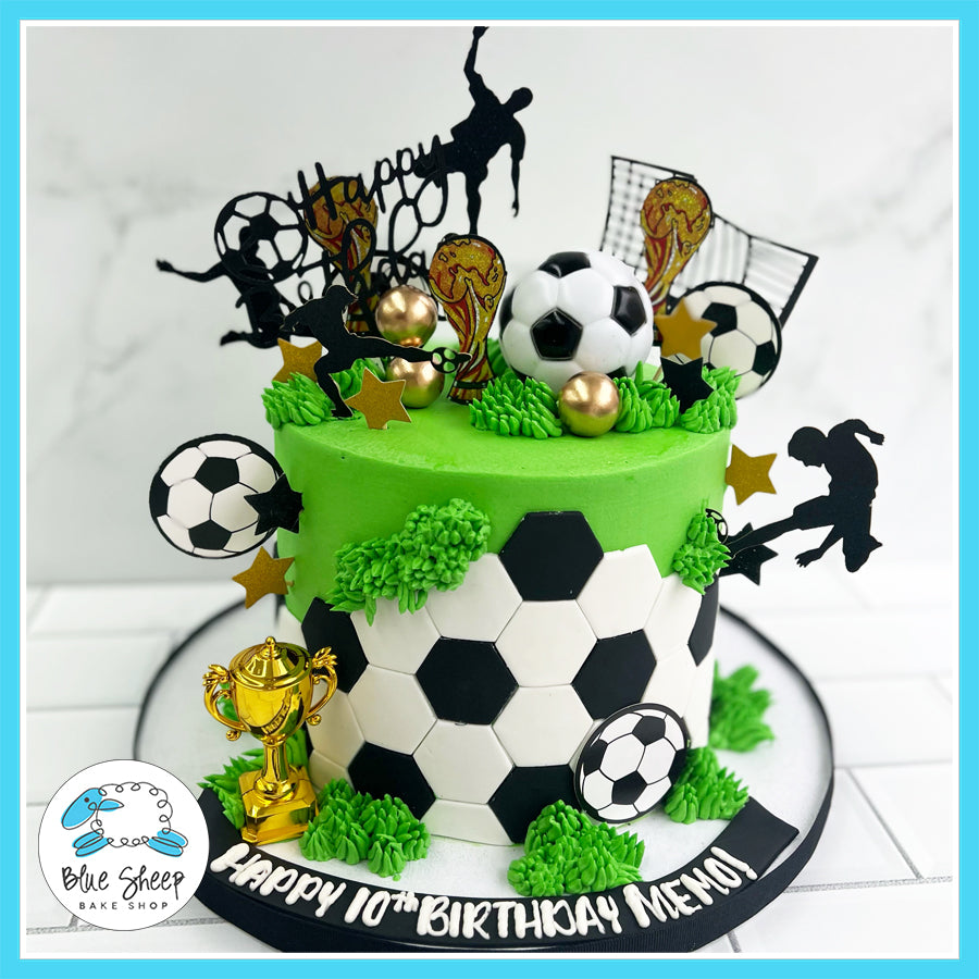 Custom soccer birthday cake with green buttercream, fondant soccer ball panels, gold trophy topper, and soccer player silhouettes. Made by Blue Sheep Bake Shop in Somerville, NJ.