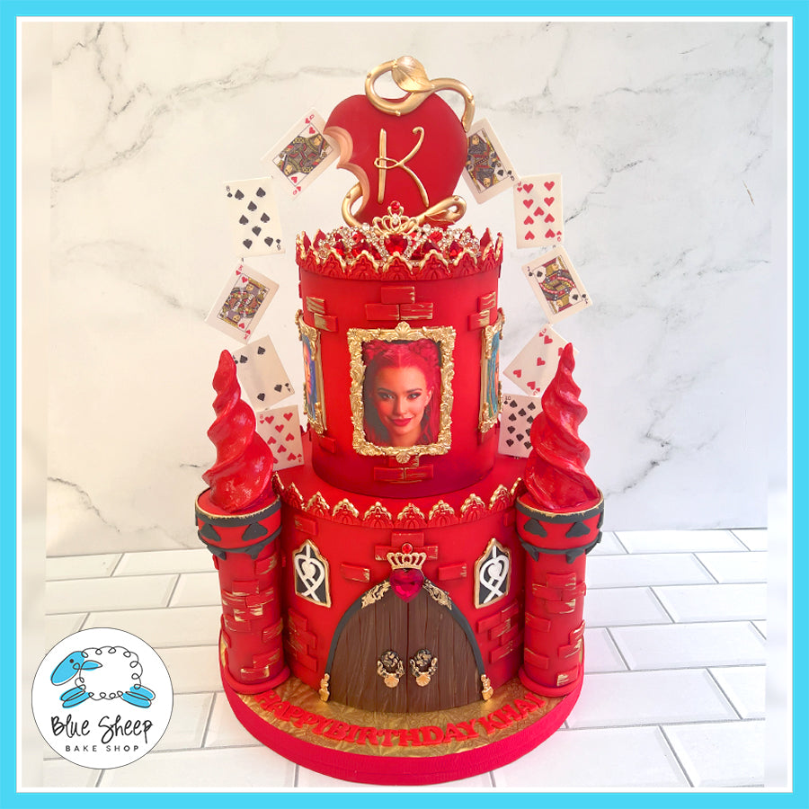 Red castle-themed cake with gold accents, playing card decorations, and an edible portrait.