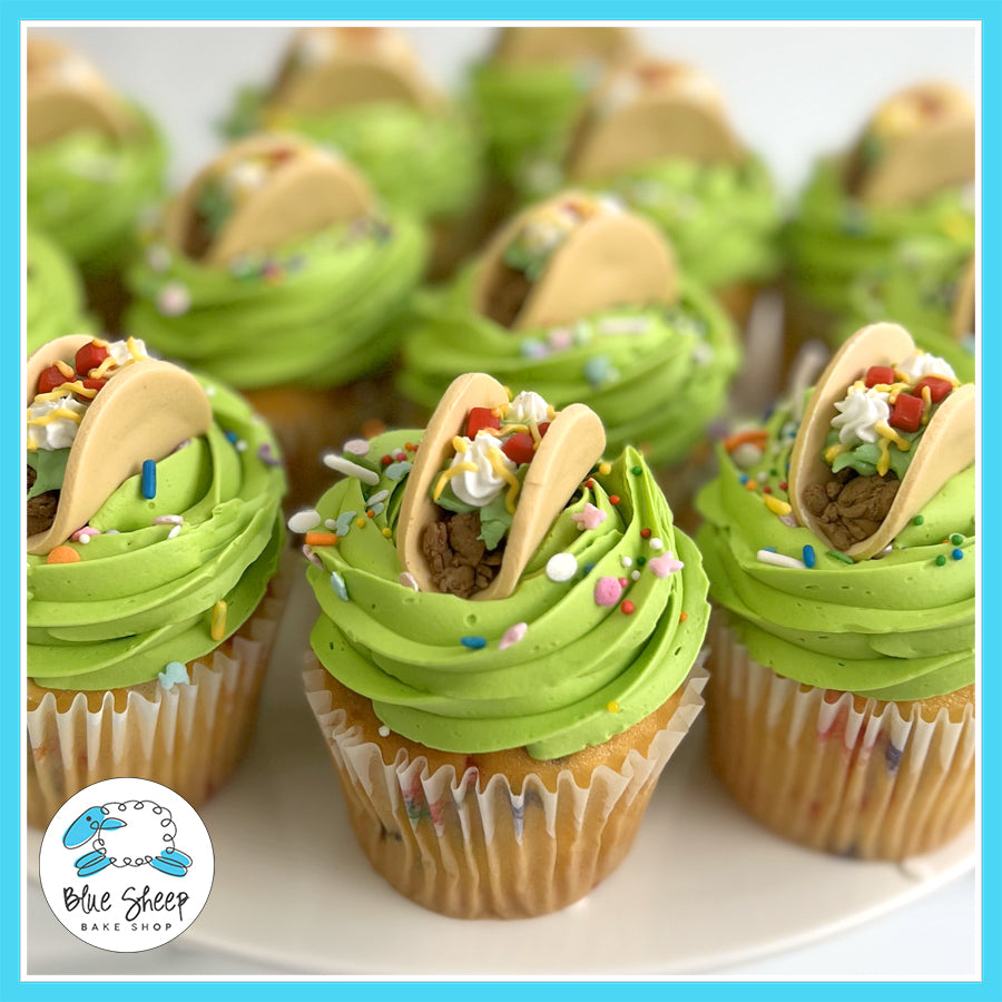 Cupcakes with green frosting topped with mini taco decorations and colorful sprinkles.