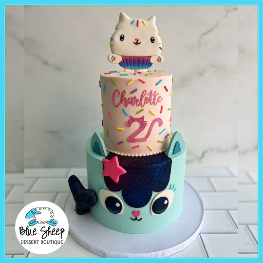 Gabby's Dollhouse themed custom birthday cake with two tiers, featuring a cat face, sprinkles, and a kitty cupcake topper.