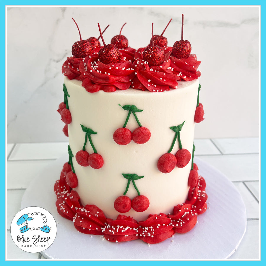 Cherry-themed birthday cake with hand-piped cherries, red buttercream swirls, edible glitter cherries, and white pearl sprinkles.