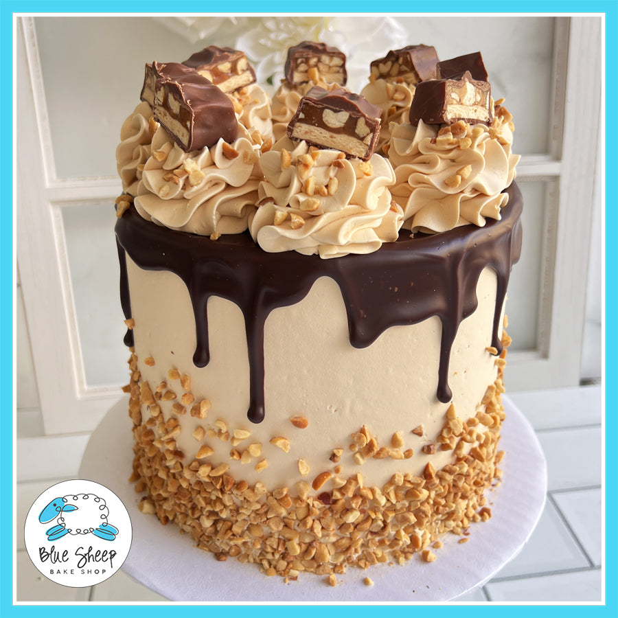 Gourmet Snickers-inspired cake with chocolate drip, caramel buttercream, peanuts, and Snickers bar toppers by Blue Sheep Bake Shop in Somerville, NJ.