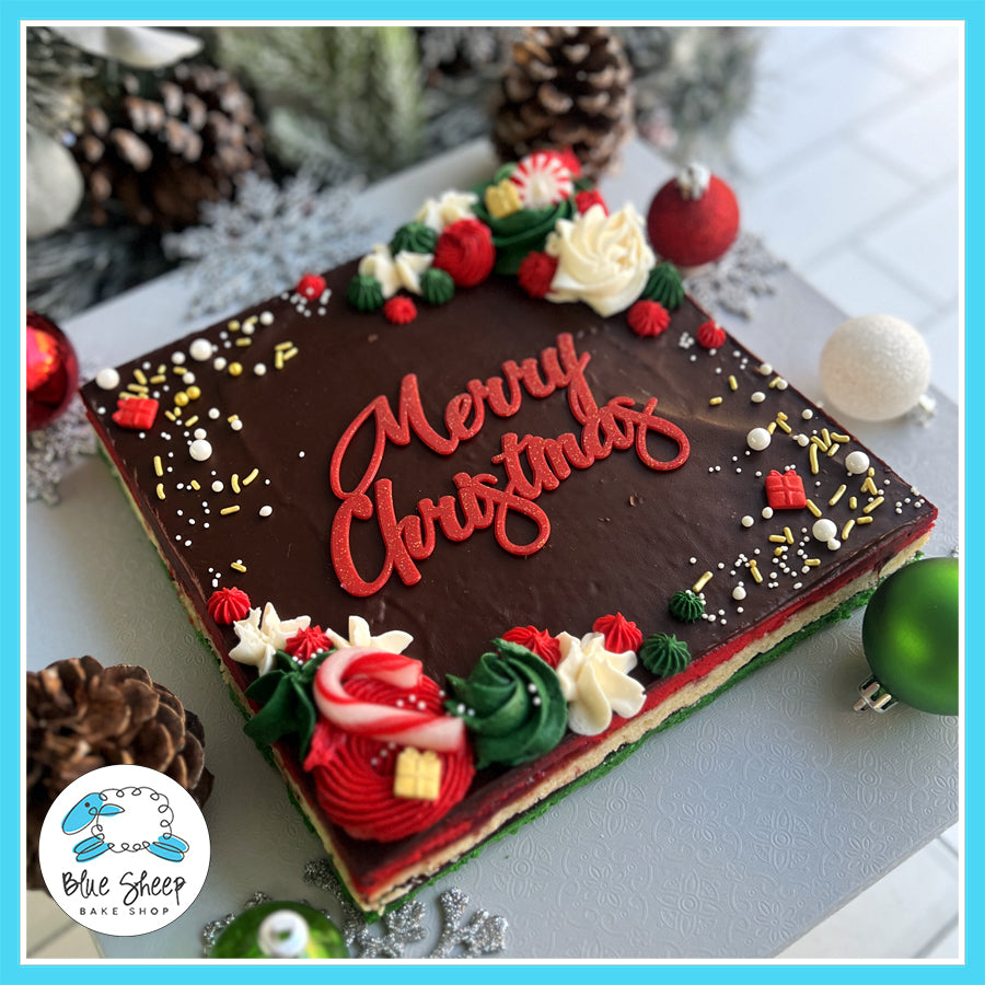 Italian Rainbow Cookie Cake with chocolate ganache and holiday decorations, featuring "Merry Christmas" lettering, from Blue Sheep Bake Shop.