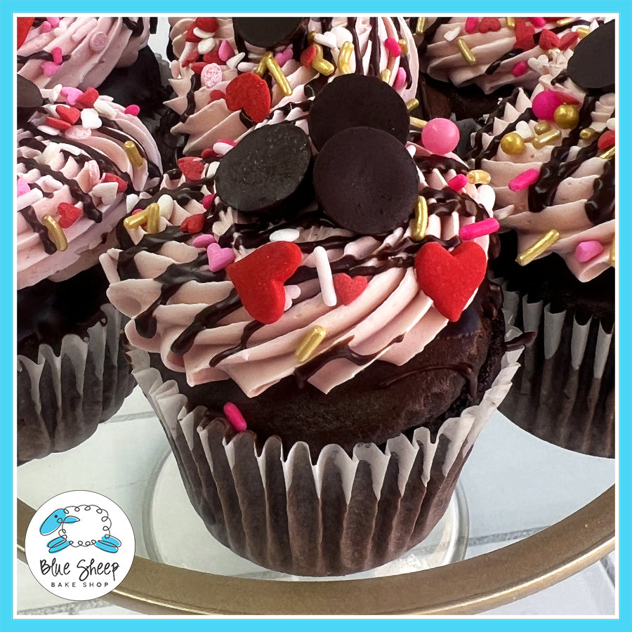 Decadent Valentine’s Day chocolate cupcake filled with raspberry, dipped in ganache, and topped with raspberry Swiss buttercream, ganache drizzle, and sprinkles.