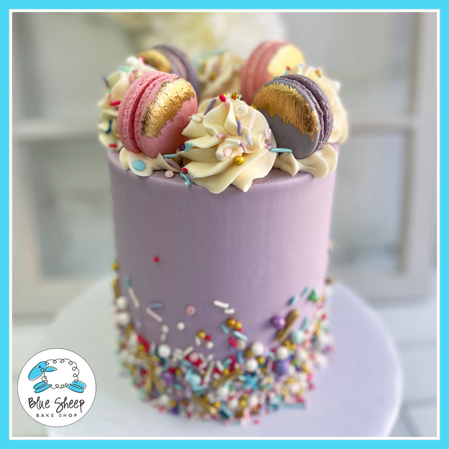 Lavender birthday cake with gold-accented macarons, buttercream swirls, and colorful sprinkles by Blue Sheep Bake Shop.