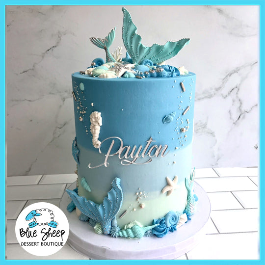 Seaside Elegance Mermaid custom cake with blue gradient, mermaid tails, seahorses, seashells, starfish, and personalized name decoration.