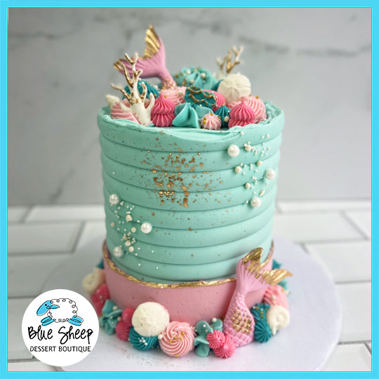 A teal and pink birthday cake with a mermaid tail, seashells, and coral decorations.