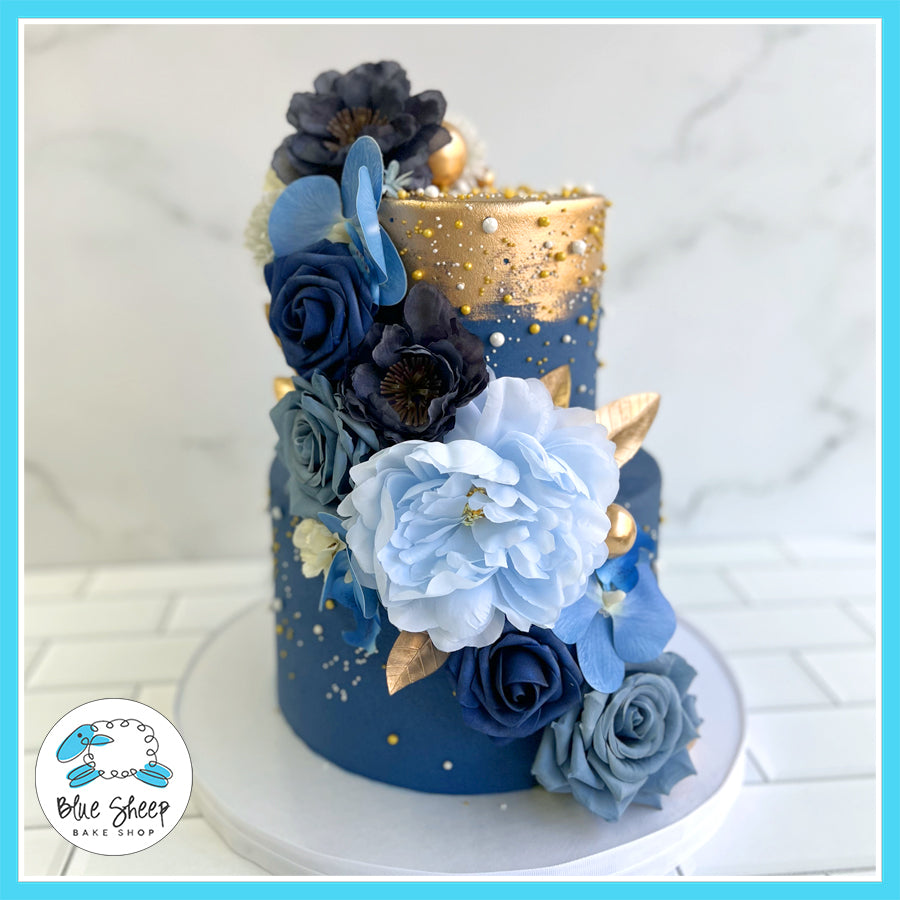 Two-tier navy blue and gold cake with cascading blue, black, and gold flowers.