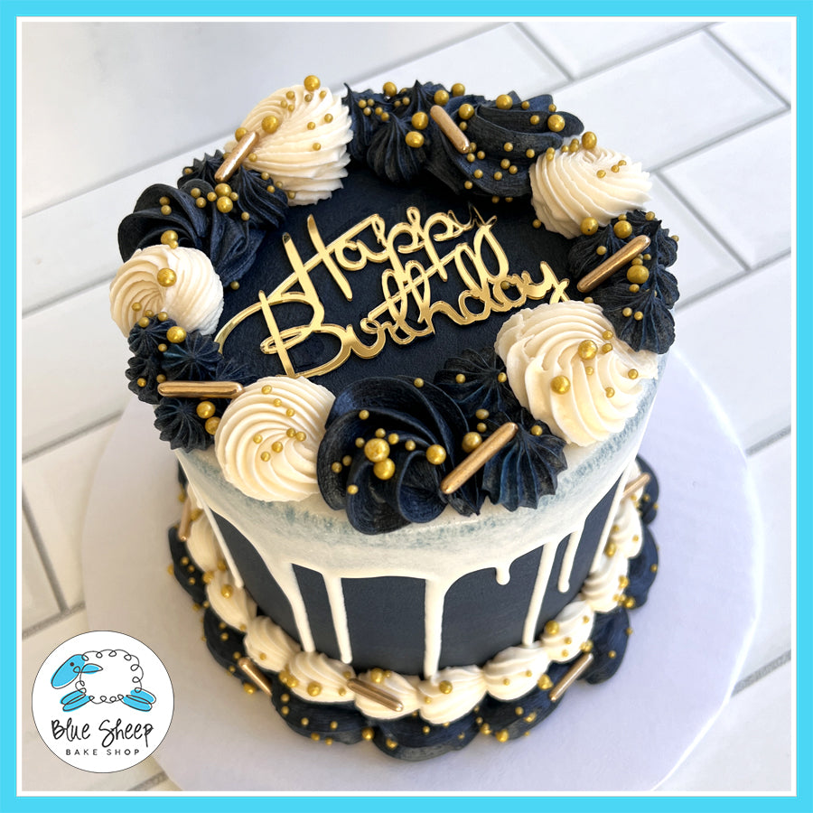 Elegant navy and gold birthday cake with white chocolate drip, buttercream swirls, gold sprinkles, and a “Happy Birthday” topper, available at Blue Sheep Bake Shop in Somerville, NJ