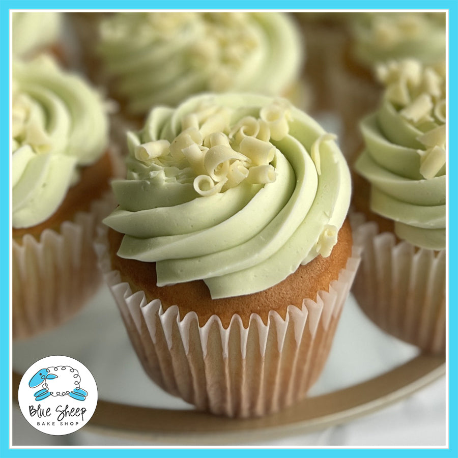 Pistachio cupcakes with cherry filling, frosted with pistachio buttercream and garnished with white chocolate curls.