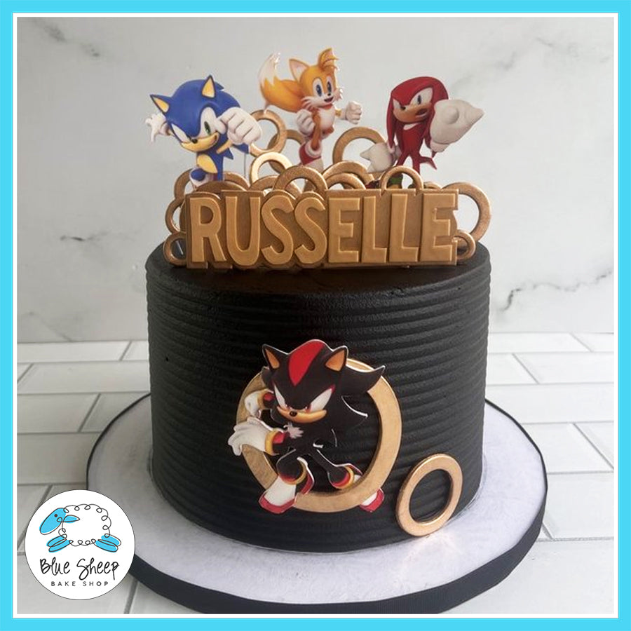 Custom Sonic the Hedgehog birthday cake featuring Sonic, Tails, Knuckles, and Shadow with a black and gold design, golden rings, and a personalized topper.