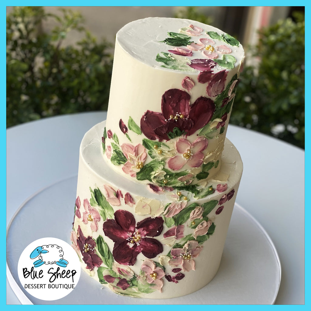 Two-tiered bridal shower cake with hand-painted bordeaux and blush floral buttercream design, adorned with delicate piped flowers and elegant pearl embellishments on a white background