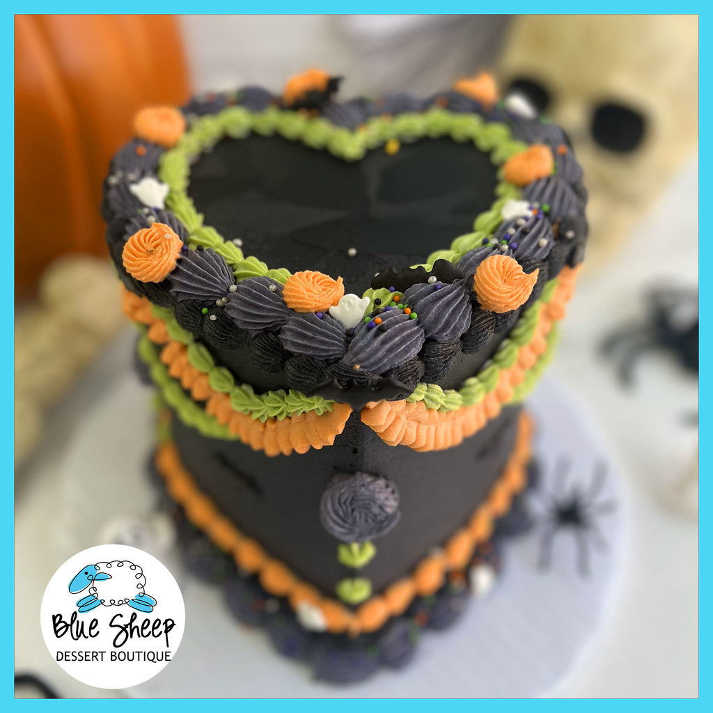 Lambeth style Halloween cake, heart-shaped bakery cake with black buttercream, and piping in green, orange, and grey tones. Decorated with Halloween themed sprinkles and little sugar ghosts.
