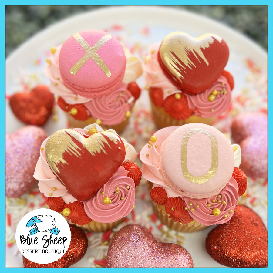 Valentine's Day themed cupcakes with pink frosting, decorated with gold accents, 'XO' macarons, and edible pearls,