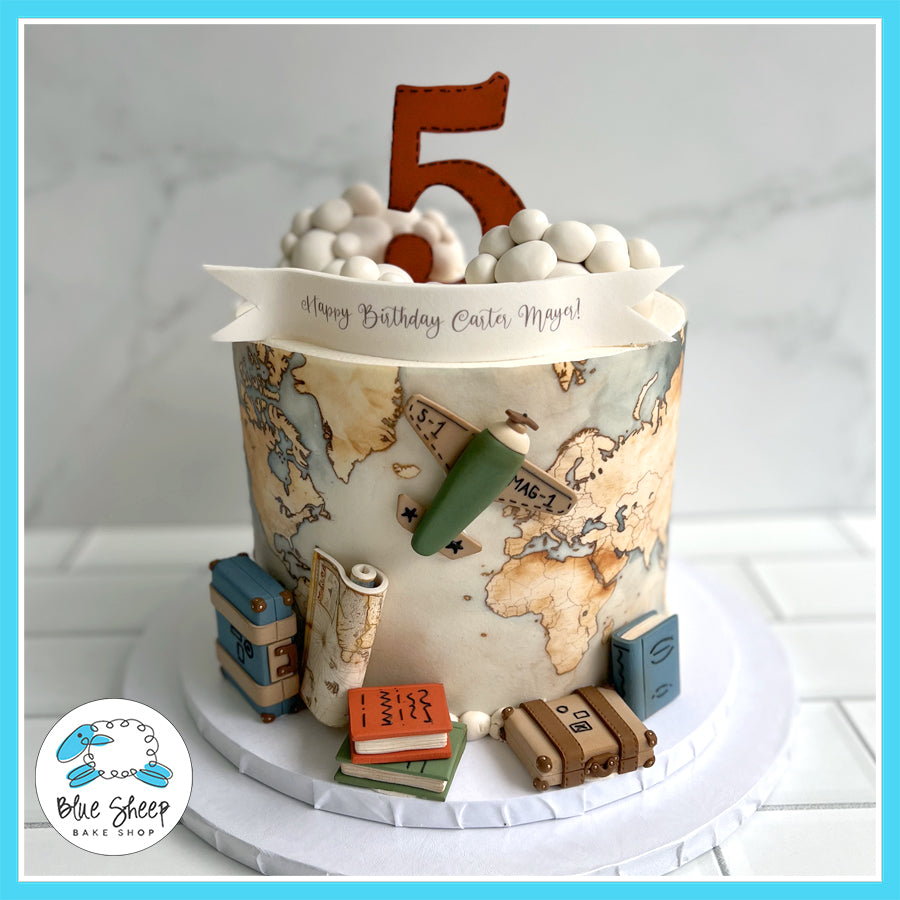 World Traveler Birthday Cake with a world map design, fondant suitcases, books, vintage airplane, and a number 5 topper